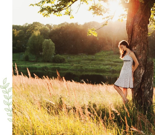 A woman standing next to a tree in the middle of a field.