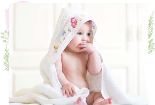 A baby wrapped in a towel sitting on the floor