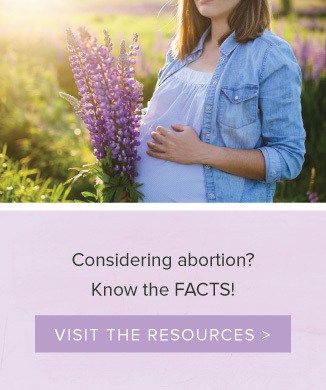 A woman holding her pregnant belly in front of some flowers.