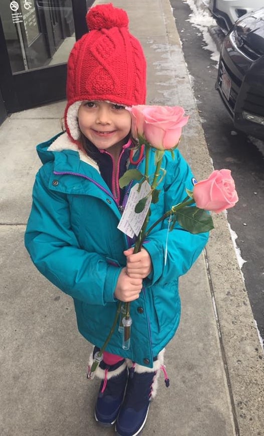 A little girl holding two roses on the sidewalk.