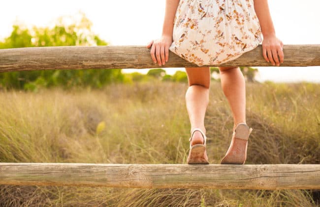 A woman in white dress standing on top of wooden rail.