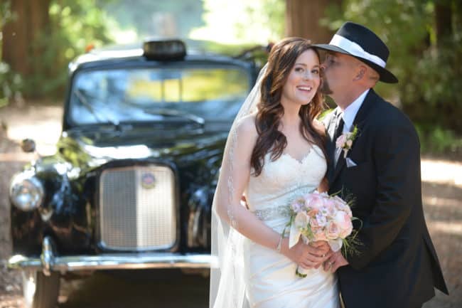 A bride and groom kissing in front of a taxi cab.