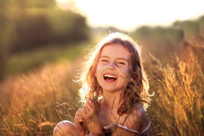 A young girl sitting in the grass smiling.