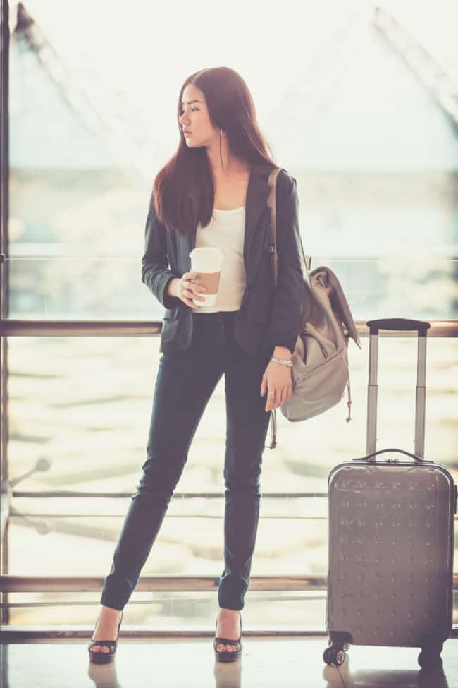 A woman standing in front of a window with luggage.