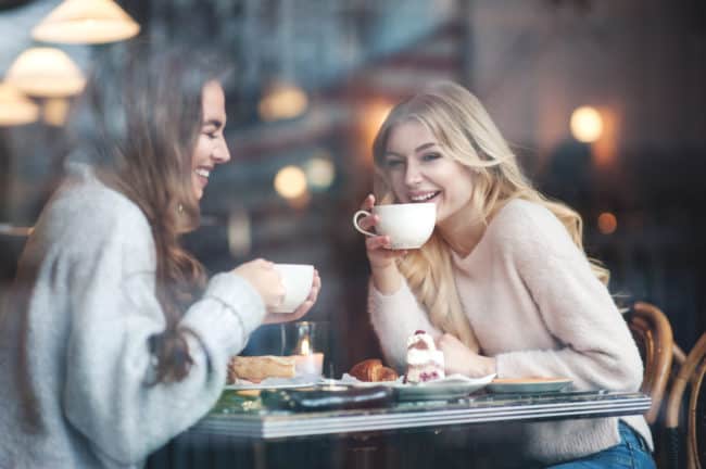 Two women sitting at a table with cups of coffee.