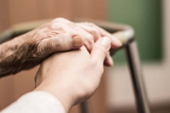 A person holding their hands over the handle of a chair.